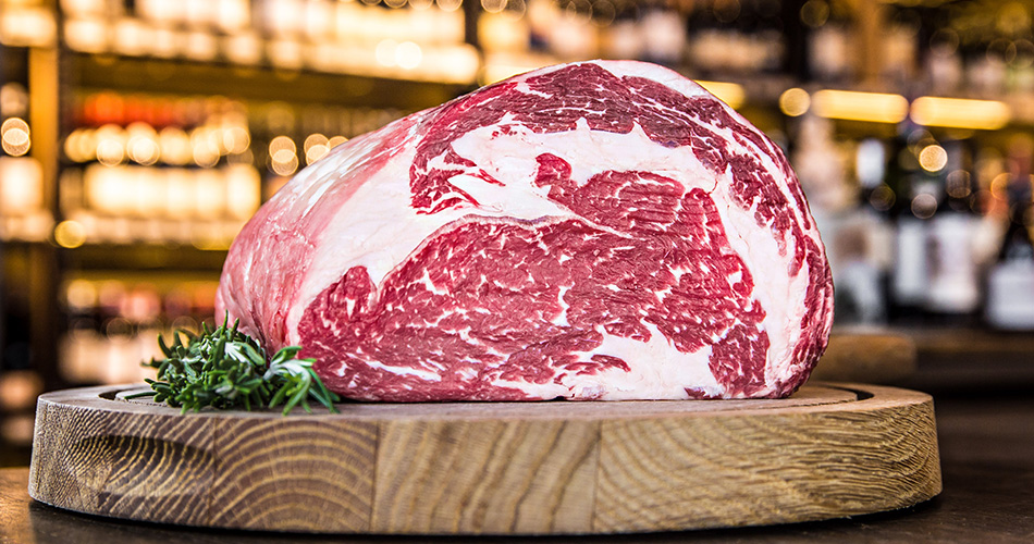 Kategorie Premium Frischeparadies Fleisch Ein Stück Premium Rindfleisch mit schöner Fett Marmorierung serviert auf einer runden Holzplatte.
